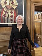 A woman with blonde hair wearing a tartan scarf and black coat.
