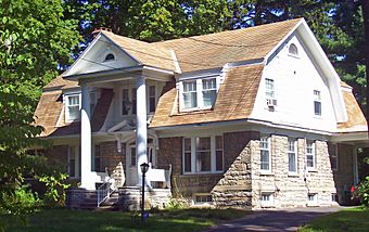A two-story stone house with a tan asphalt shingle roof and columns on the front