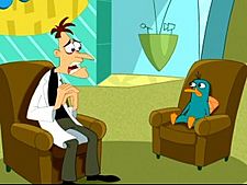 A cartoon Caucasian man wearing a white lab coat sits on a brown coach with a sad and sincere look on his face. Across from him is a green platypus bearing the same expression and on the same kind of couch. Behind them is a TV set with blue walls and a large yellow sign.