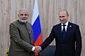 Two standing men are pictured shaking hands. The first is dressed in Indian clothing; the second is in a Western business suit; both standing behind a Russian flag.