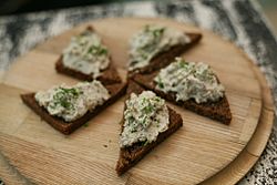 Five triangular slices of rye bread topped with vorschmack lying on a wooden place