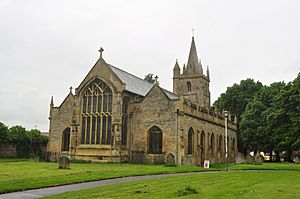 A stone church seen from the north east, with a large Perpendicular east window, aisles with pinnacles, and a west tower with pinnacles and a spire