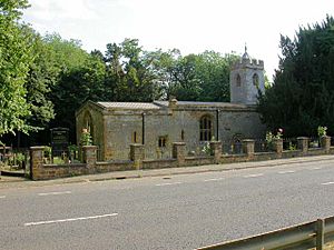A stone church with a tower on the right.  This has a battlemented parapet beyond which is a small pyramidal roof.