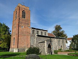 A church seen from the southwest with a large brick tower on the left and the flint body of the church on the right, showing the clerestory, south aisle and porch