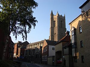 Protruding above the houses in a street is a battlemented tower with a corner turret, and the body of the church beyond it