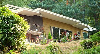 Photograph of a flat-roofed house elevated on a slope in a wooded setting