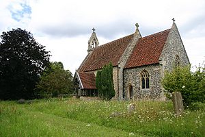 A flint church with red tiled roofs seen from the southeast; a double bellcote is at the far end