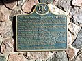 A blue plaque on a stone wall. The plaque has a yellow border, and is mostly rectangular in shape, with the long end oriented horizontally. However, the top side has a camel hump in the centre, with a circle centred at the top of the hump. Inside the circle is an Ontario coat-of-arms. The plaque reads: THE MACDONALD CARTIER FREEWAY This plaque commemorates the completion of the Macdonald-Cartier Freeway (Highway 401), the longest freeway operated without tolls by a single highway authority in North America. Covering 510 miles between Windsor on the Canada–US border and the Ontario-Quebec boundary, it serves the richest economic region in Canada. In January 1965, it was named by The Honourable John Robarts, Premier of Ontario, in honour of the two founding architects of the Confederation of Canada, Sir John A. Macdonald and Sir George-Étienne Cartier. This site is located on the last section of construction, consisting of 15 miles between Ivy Lea and Highway 2, which was completed on October 11, 1968.