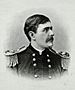 Head and shoulders of a white man with dark hair and a mustache, wearing a double-breasted military jacket with fringed shoulder boards.