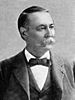 A white man with a full mustache in a dark suit with a bow tie and vest, looking right.