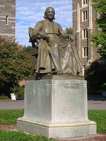 Photograph of the statue with a blue sky and stone buildings in the background