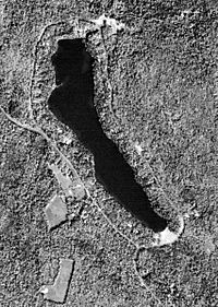 Black and white aerial view of a narrow lake ringed by a road