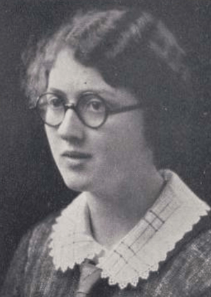 A young white woman with wavy dark hair and round glasses, wearing a rounded collar with scalloped edges