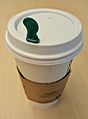 Hot Stopper in the lid of a paper coffee cup with a cardboard sleeve