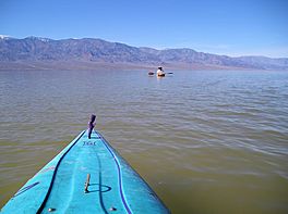 A man kayaking in a brown lake, mountains in the background, a kayak in the foreground