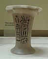 Photograph of a small white vase with black hieroglyphs on it