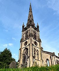 An elaborately decorated tower in light stone with dark stone dressings, windows of varying shapes and sizes, pinnacles, and a spire