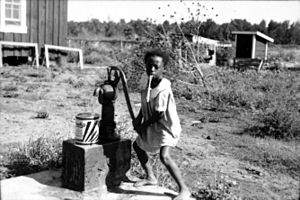 A young Black girl operates a water pump at Delta Cooperative with balloon in her mouth