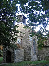 The west end of a Georgian church seen through trees, showing a porch over which is a window and a bellcote