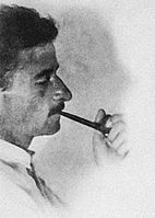 Photographic portrait of Faulkner at bust length, in profile facing right, smoking a pipe, with short hair and a mustache.