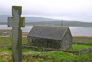 small stone chapel with cross overlooking a loch