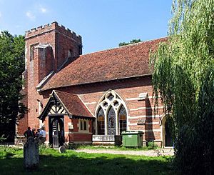 A red brick church with white stone banding and a red tiled roof seen from the southeast, showing the body of the church with a large window, a porch, and a battlemented tower