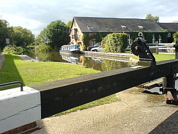 A canal lock in the sunshine.  Behind the lock is a Victorian brick building, formerly a pumping station, now a private residence.