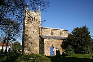 A stone church seen from the south with, on the left, an embattled tower with pinnacles, and to the right a nave with clerestorey, aisle, and pointed doorway
