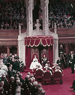 Queen Elizabeth II and Prince Philip sit on thrones before a full Parliament