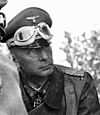 The head and torso of a man wearing a military uniform and overcoat; an Iron Cross is displayed at the front of his uniform collar.