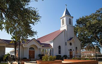 Medium sized white church with small steeple and red roof surrounded by some plant beds with brick borders.