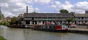 Water with two narrow boats and bridge. On the far side is a white coloured building displaying a banner which says Canal Museum and Shop.
