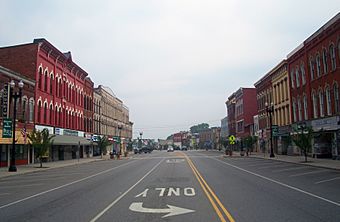 A view down the center of a wide street with three-story ornate brick commercial buildings in a mix of colors on either side. At bottom center is an upside down "Only" above a curved arrow pointing right.