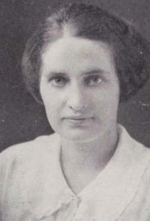 A young white woman with dark hair parted off-center and wearing a white blouse with a large collar