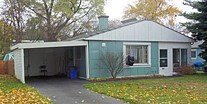 A similar blue-green gabled house with grid-pattern metal siding and a carport on the left