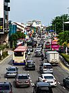 A city street lined with shophouses, with cars, lorries, motorcycles and a bus on the road.