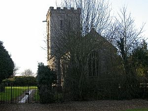 A stone church seen from the east, partly obscured by trees, with a battlemented parapet at the back