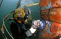 Diver wearing a diving helmet is sanding a repair patch on a submarine