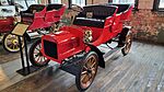 A red-colored, old-fashioned car with two seats and brass fittings