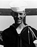 A black and white image of Ray in his military uniform with hat. His head is ducked down slightly and he is smiling at the camera.