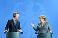 Macri and Angela Merkel, smiling at separate podiums