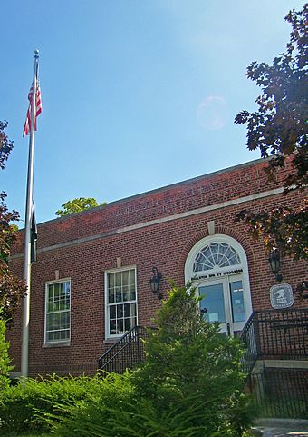 View of some of the front of the post office with a flagpole in front and some lens flare in the blue sky