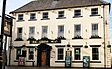 Front of a three-storey building, six windows across, with a large-framed wood door at ground level and a painted sign with the words "THE QUEENS HEAD"