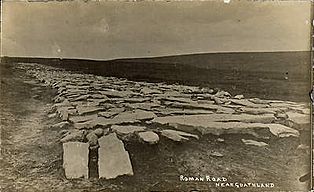 Photograph of Wade's Causeway, taken in approximately 1912 and showing a relatively even surface of large, broad, flat stone slabs raised on a small embankment a couple of feet above the surrounding moor.