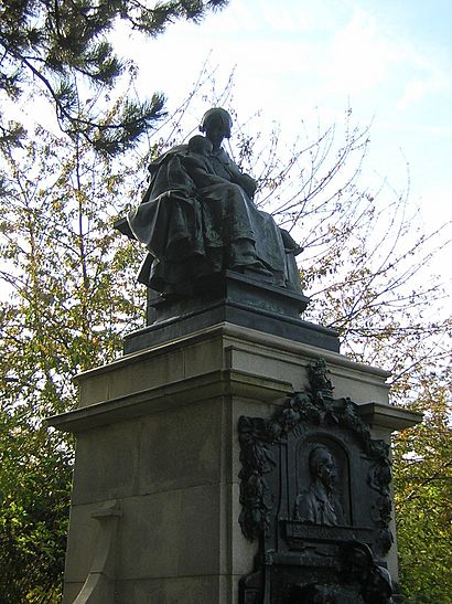 A statue on a high plinth of a woman holding two children. The plinth has a bust of Thomas Barnardo above effigies of three further children. The sculptures are of bronze and the plinth is of stone.