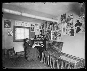 Frances Benjamin Johnston seated at a desk in her studio-office, with adverstising posters on the walls, including the Chap Book, Harper's, and Lippincott's magazines LCCN2017645690