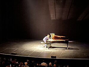 Jon Batiste reaching inside piano during improvised performance at Count Basie Theatre