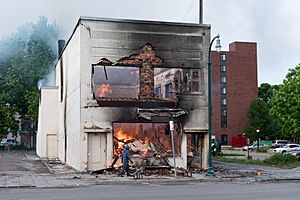 A man walks by a burning building on Thursday morning after a night of protests and rioting in Minneapolis, Minnesota (49945327763)