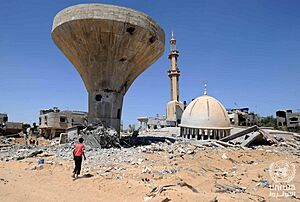 A child walking in front of a collapsed mosque and a water tower in Khuza'a, Gaza Strip.
