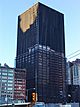 Ground-level view of a 40-story building; the highest 20 floors have a black tarp-like covering. The exterior facade has been removed from the lower 20 floors, leaving exposed steel columns visible.